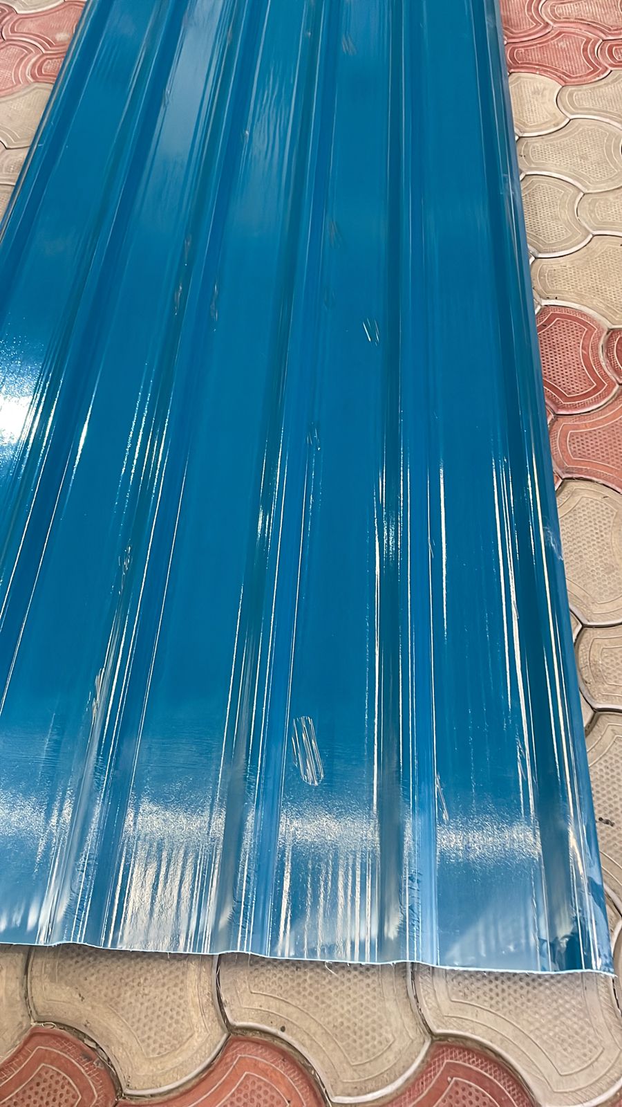Close-up of glossy blue FRP profile sheet on paved surface, showing corrugated ridges and protective film.